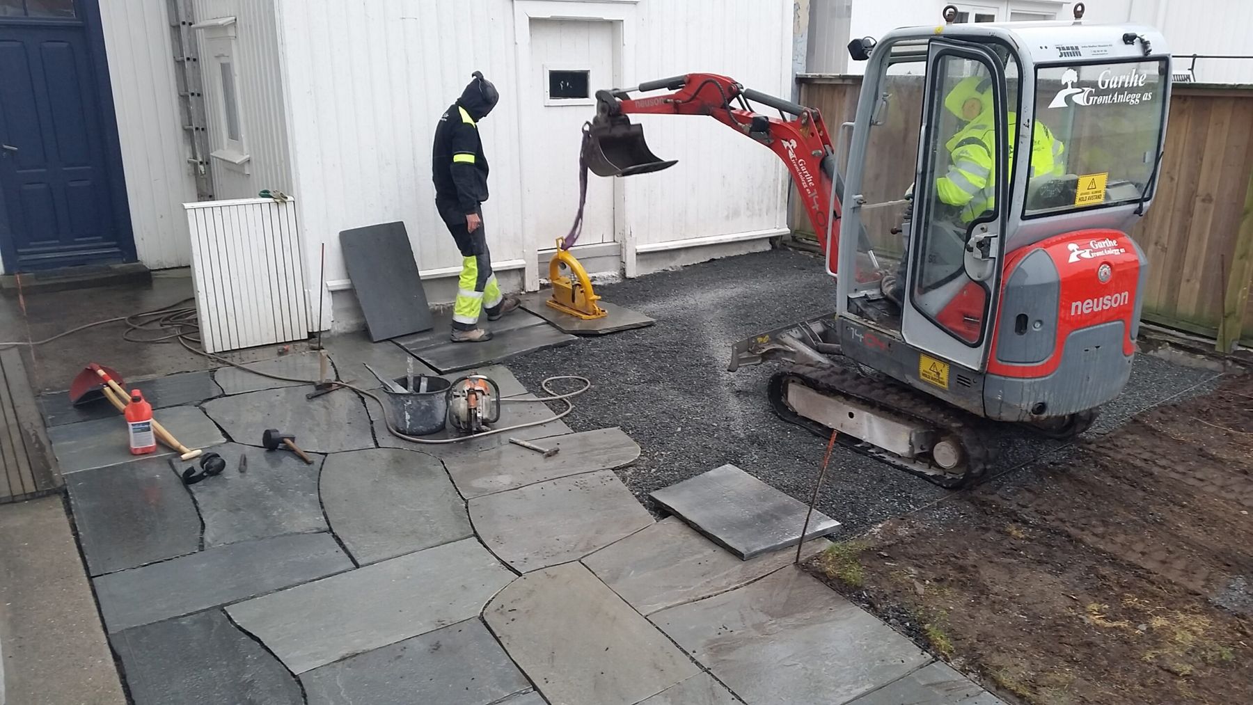 Minigraver i arbeid foran et hus