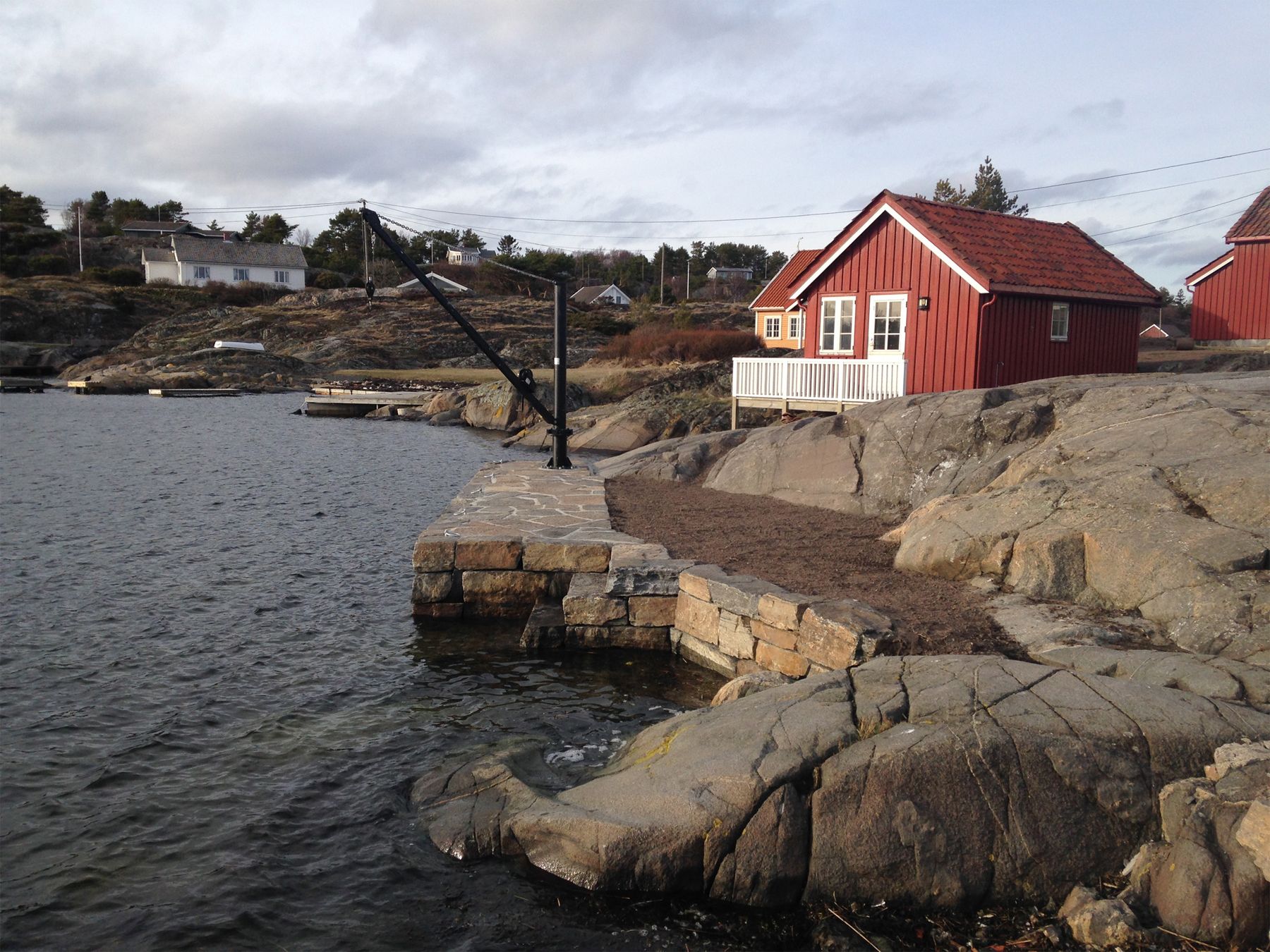 Brygge i naturstein på svaberg med sjøhus i bakgrunnen