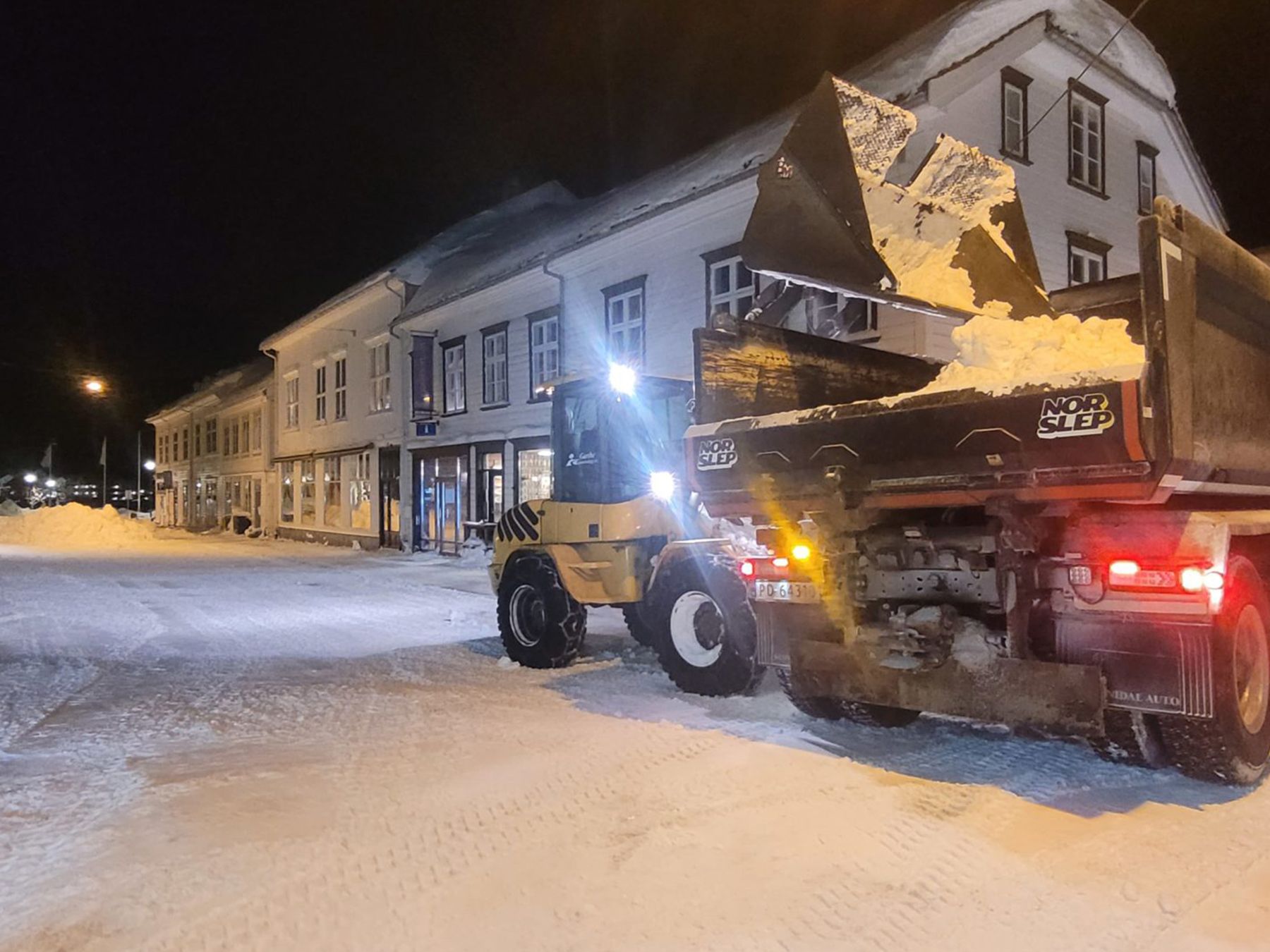 Hjullaster laster snø på lastebil i en gate