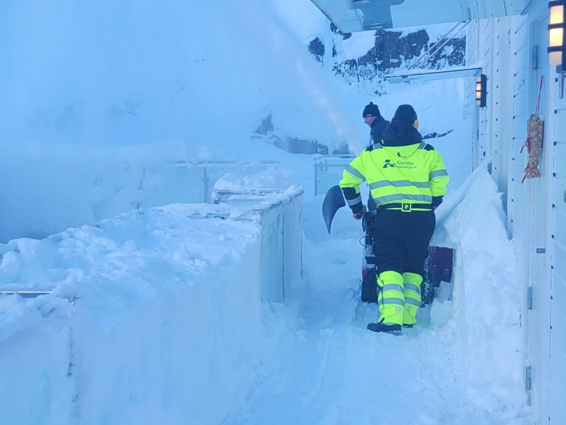 Arbeider i refleksklær måker snø for hånd
